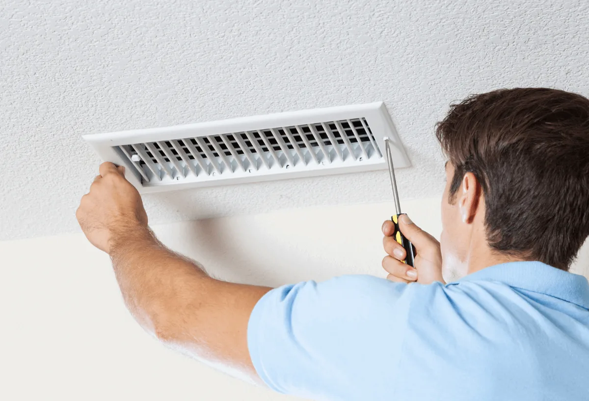 A picture of someone screwing an air duct vent into place.